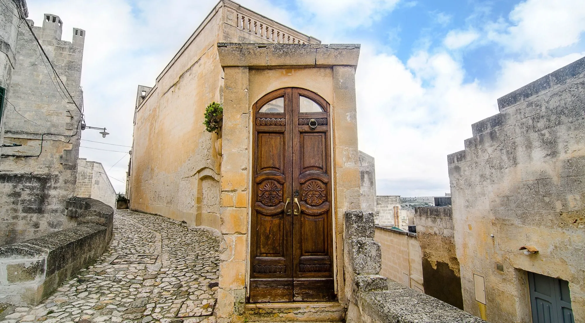 A narrow cobbled lane in the Sassi ending at an arched wooden door set in pale stone