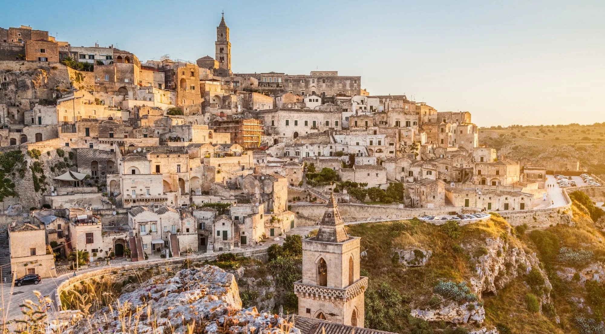 Panorama of Matera's stone houses stacked down the slope, a bell tower in the foreground and the cathedral on the skyline