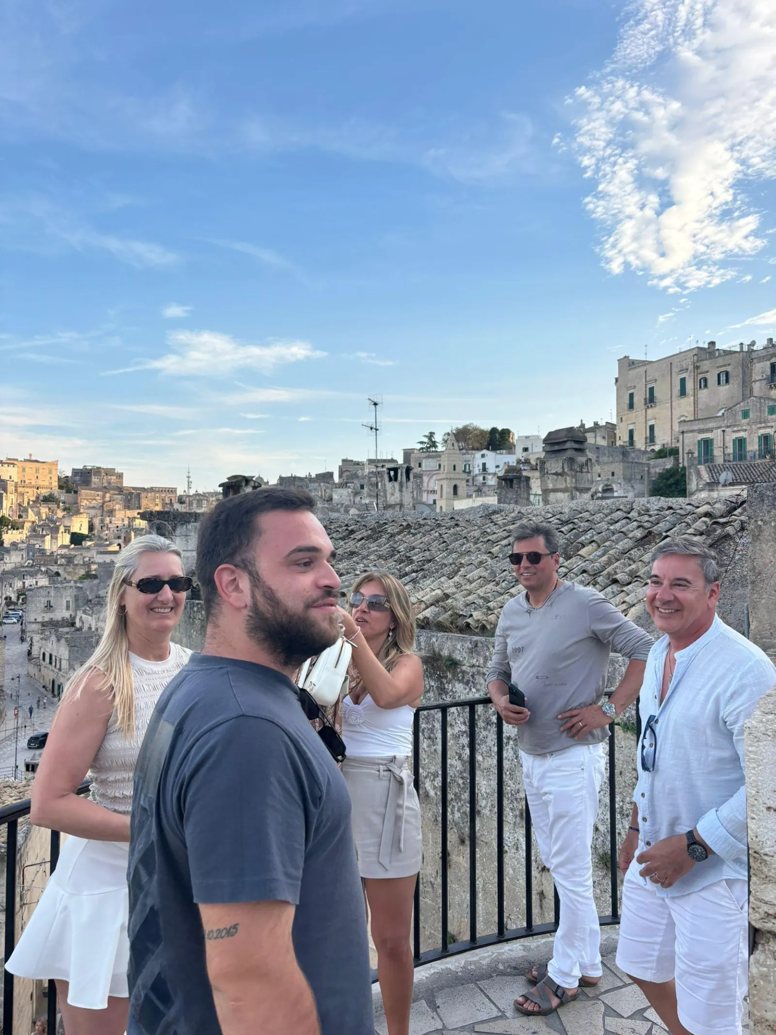 Five visitors chat at a railing on a terrace overlooking the Sassi in Matera.