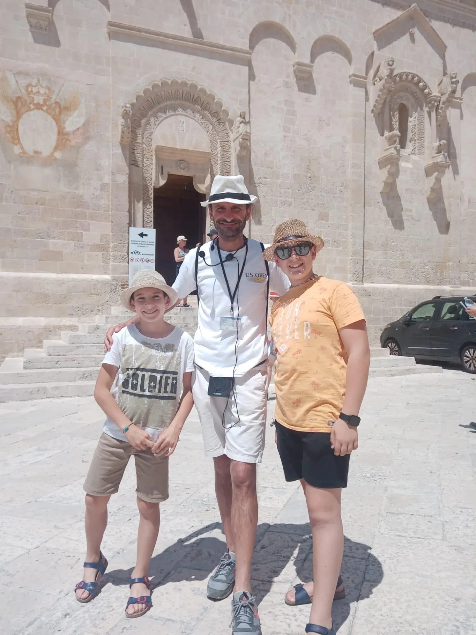 A guide and two visitors pose in front of the carved stone doorway of a church in Matera.