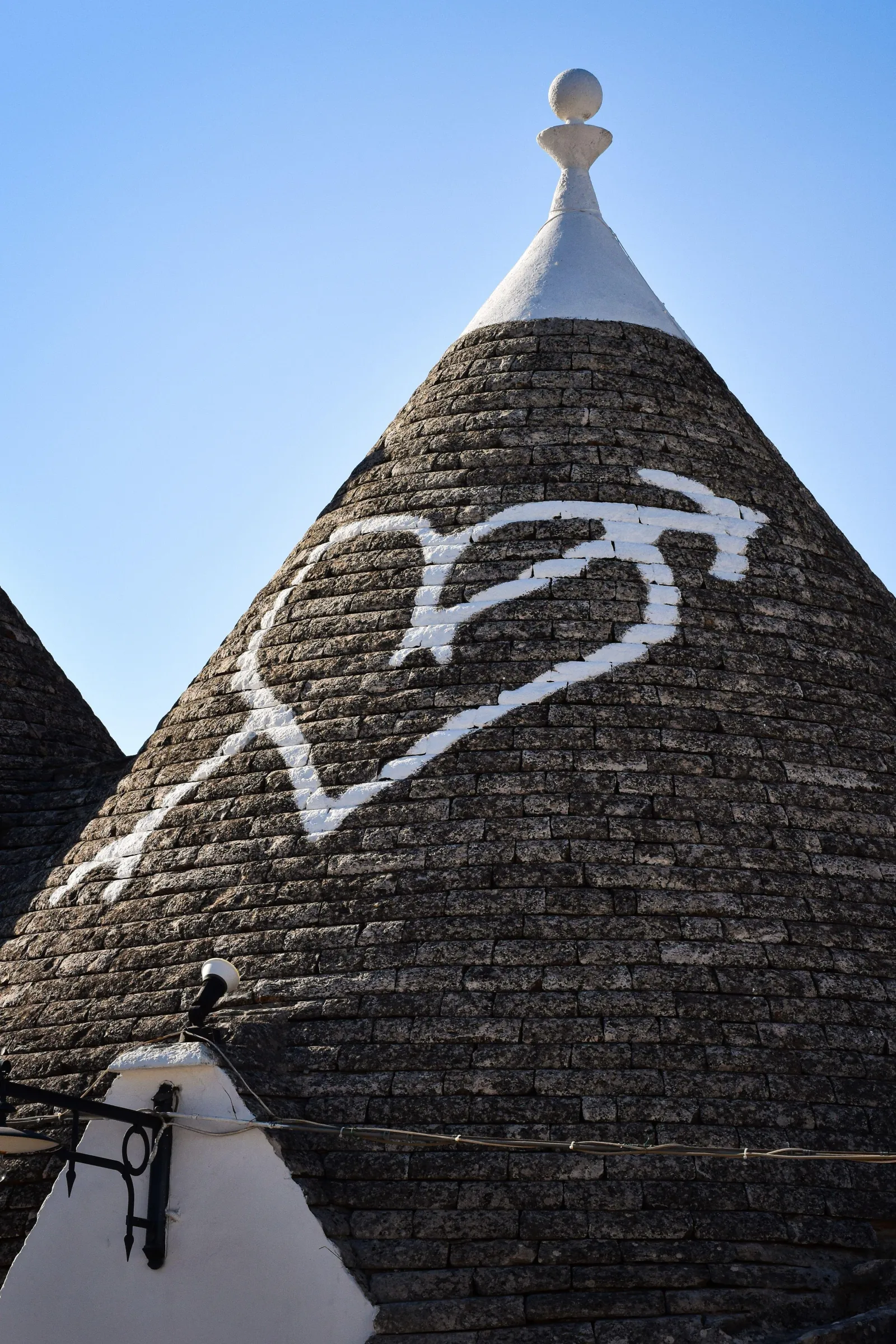 Close view of a trullo's grey conical stone roof with a white painted heart symbol in Alberobello.