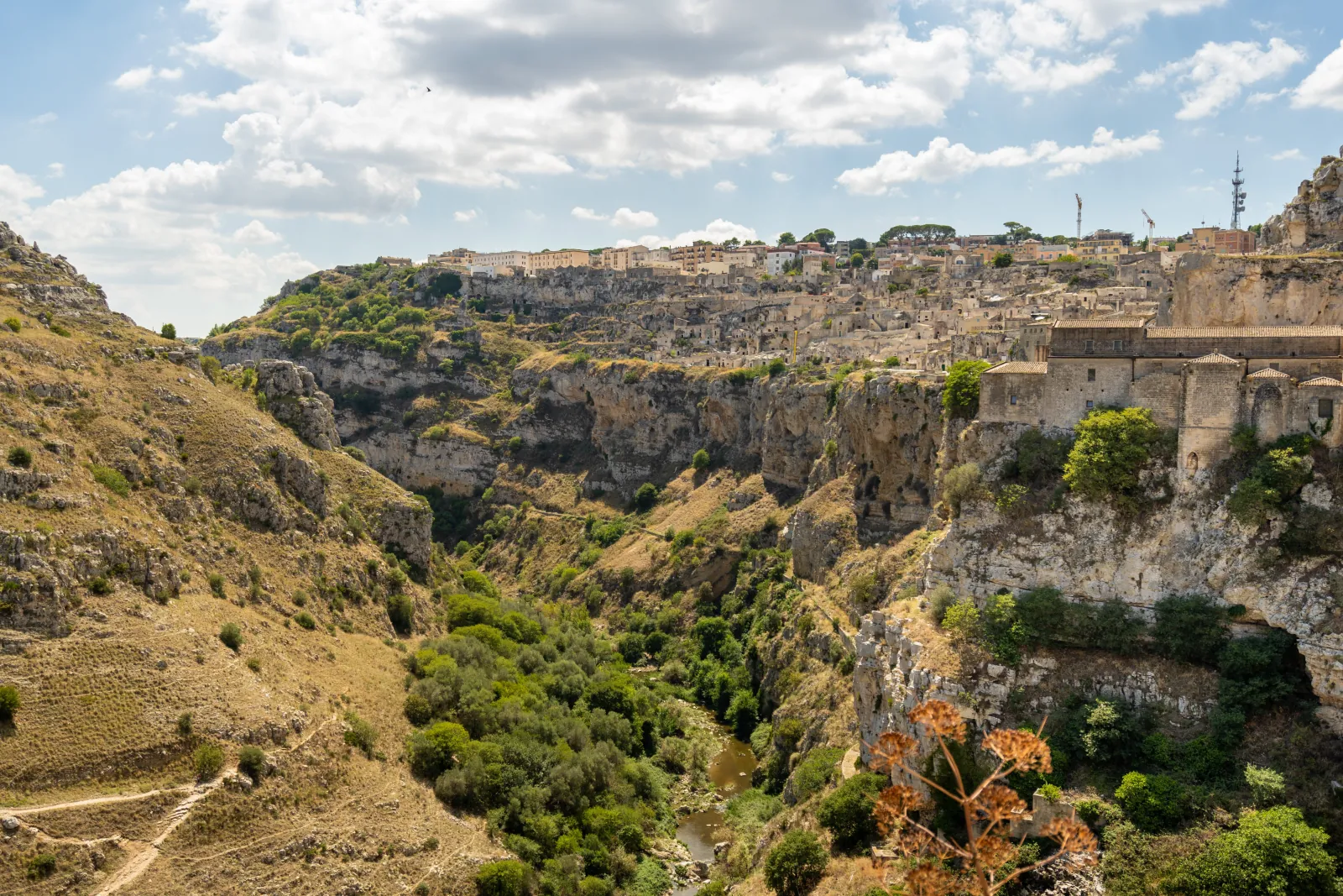 The Gravina gorge below Matera, with scrubby slopes and the stone buildings of the old town on the far rim.
