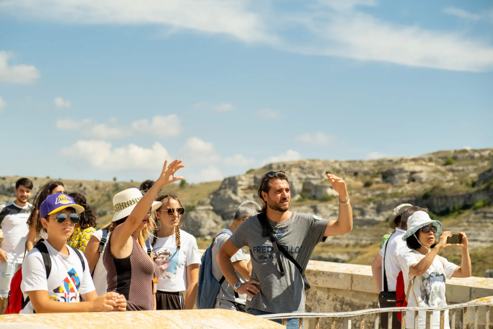 A guide raises an arm to point out sights to a group at a stone parapet overlooking the Murgia plateau.