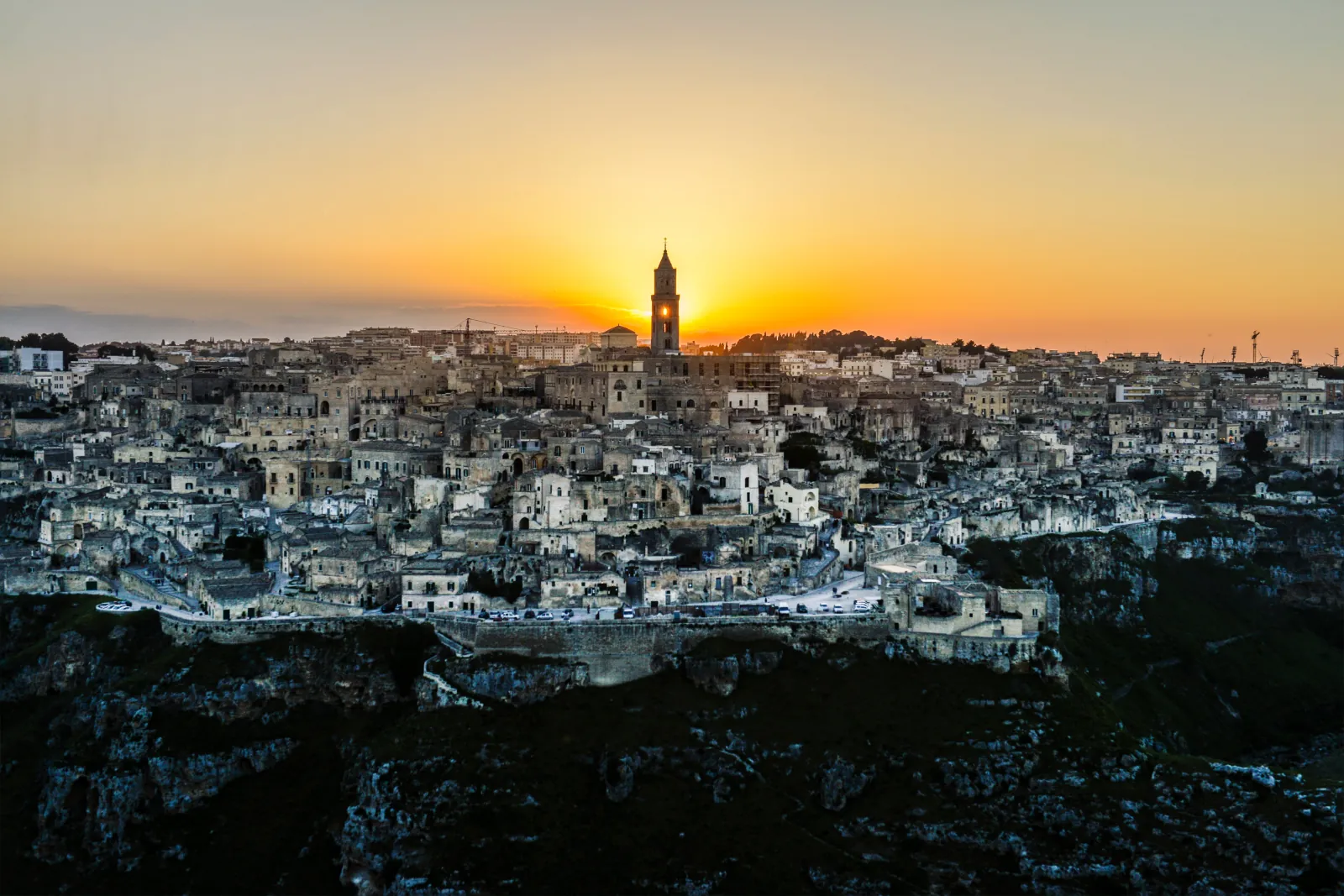 Sunset behind the cathedral bell tower and stone houses of Matera, seen from the Murgia side of the gorge.