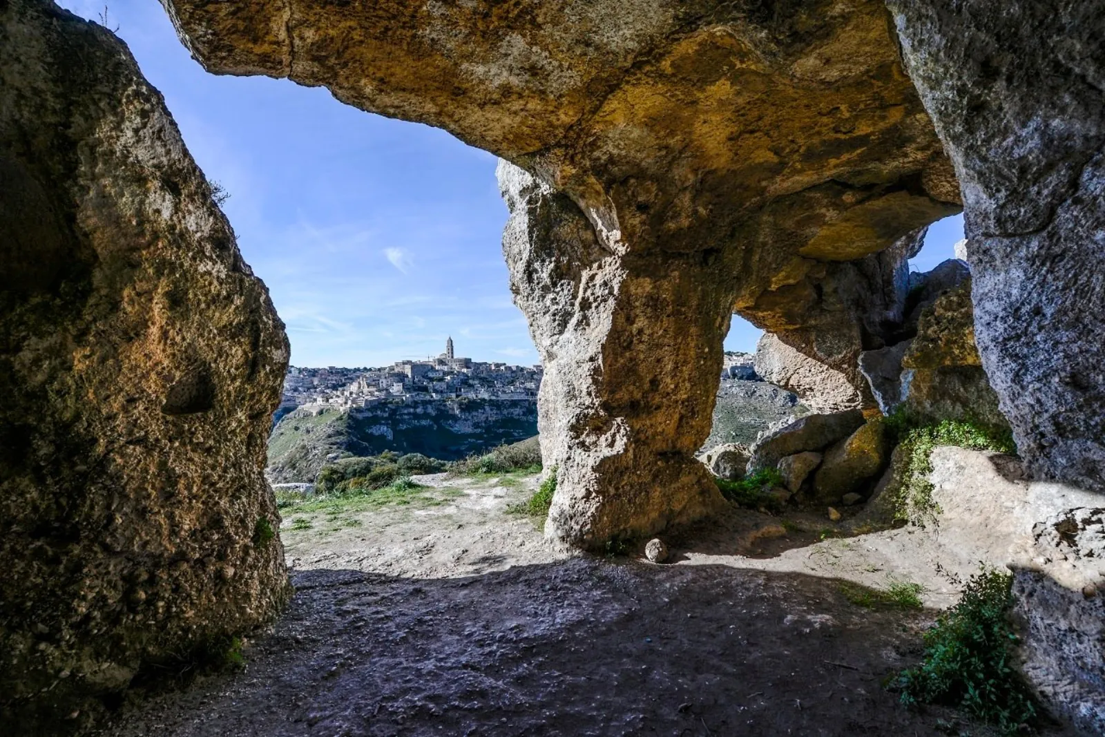 A rock arch in the Murgia limestone frames a distant view of Matera across the gorge.