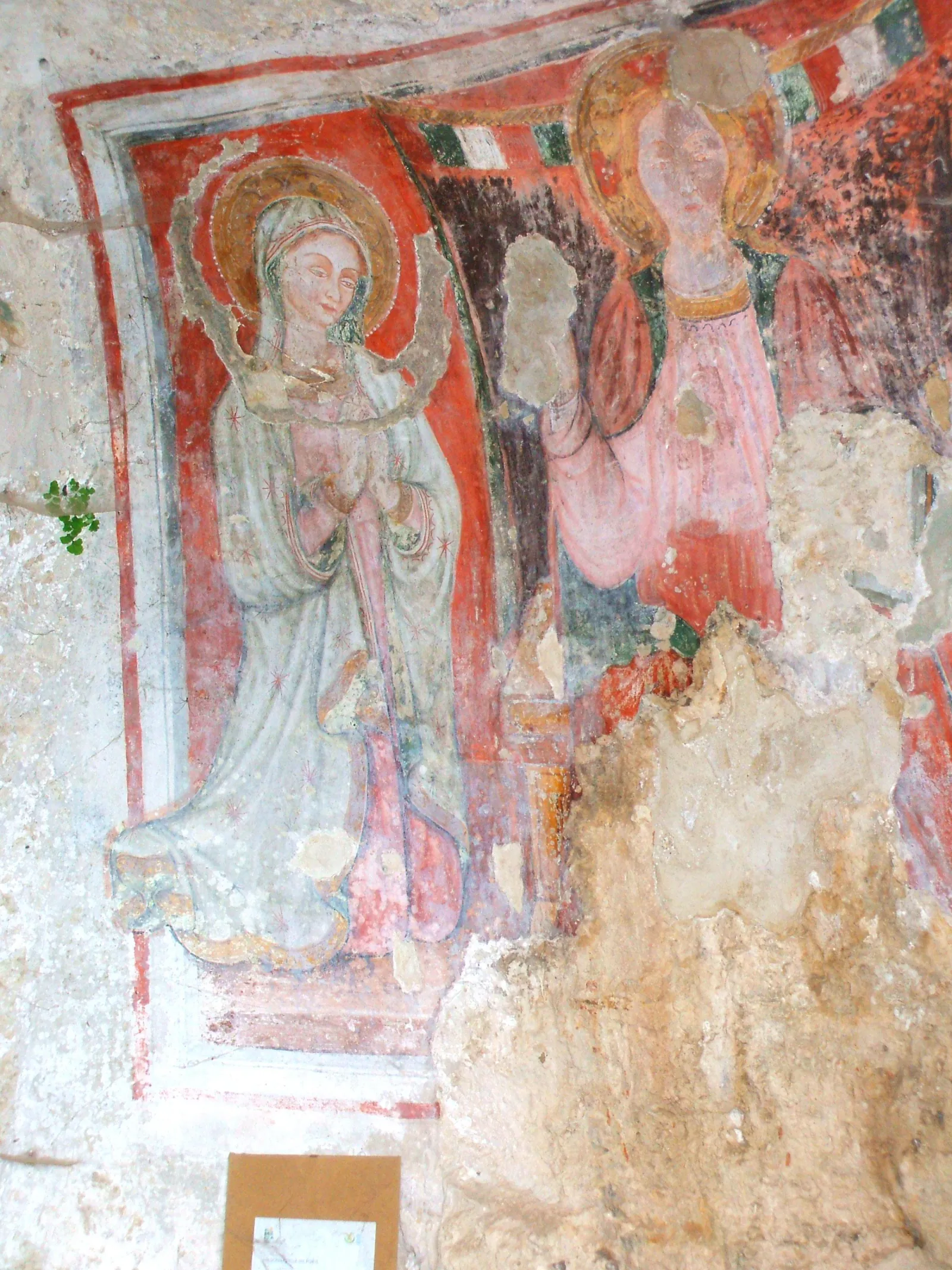 A faded red and gold fresco of the Virgin and another saint on the wall of a rock-cut church.