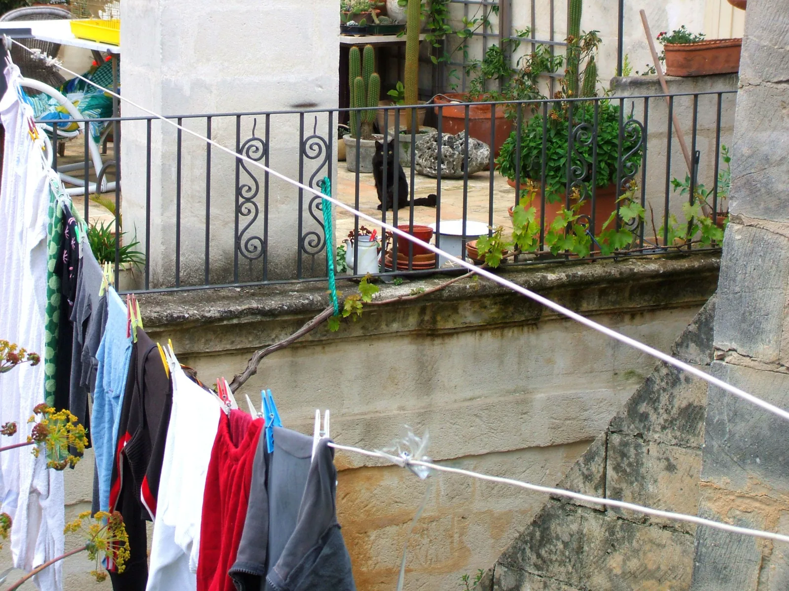 Laundry hangs on a line beside a wrought-iron balcony with potted plants on a stone house in the Sassi.