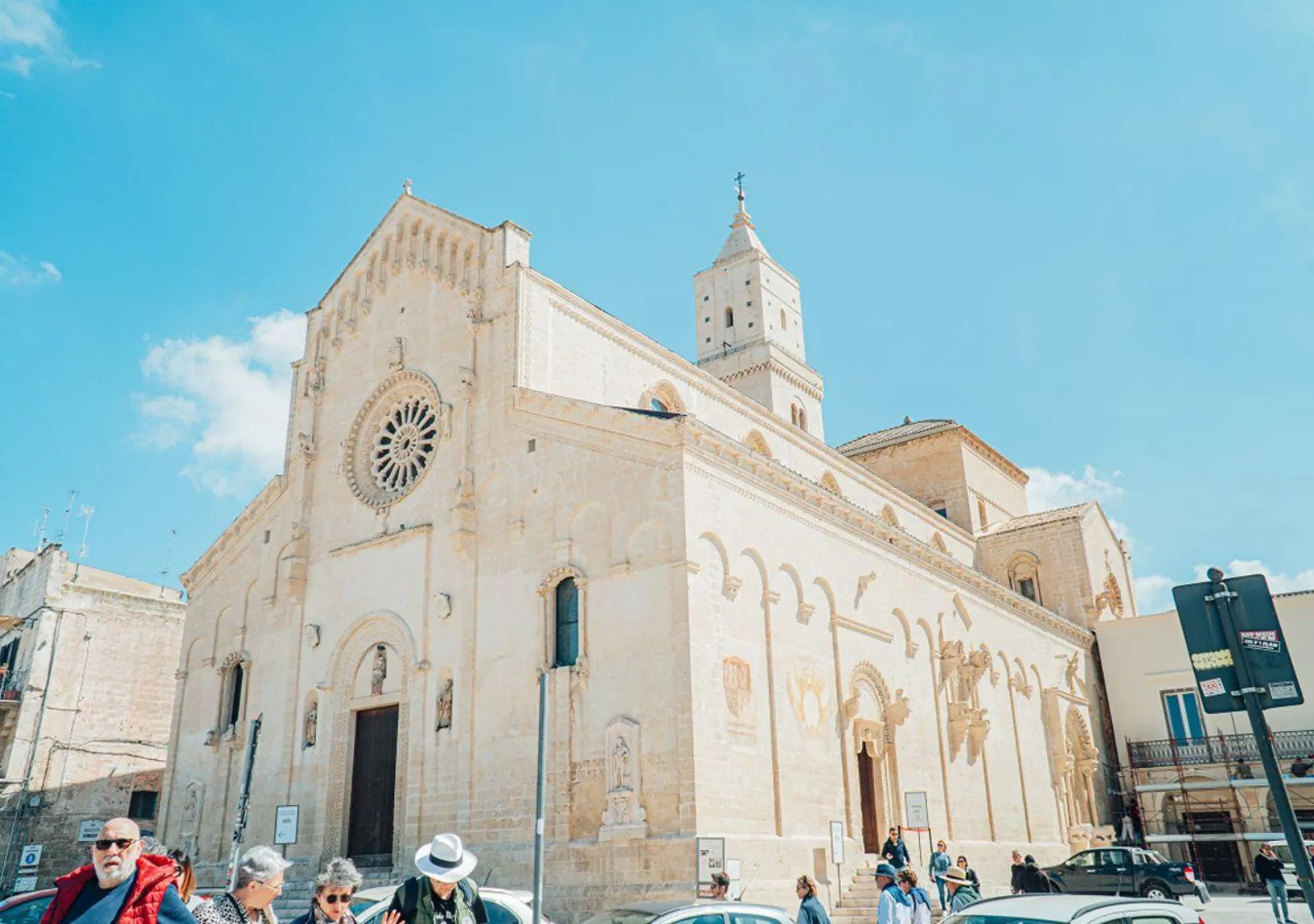 The facade of Matera Cathedral with its rose window and bell tower, seen from the side under a blue sky.