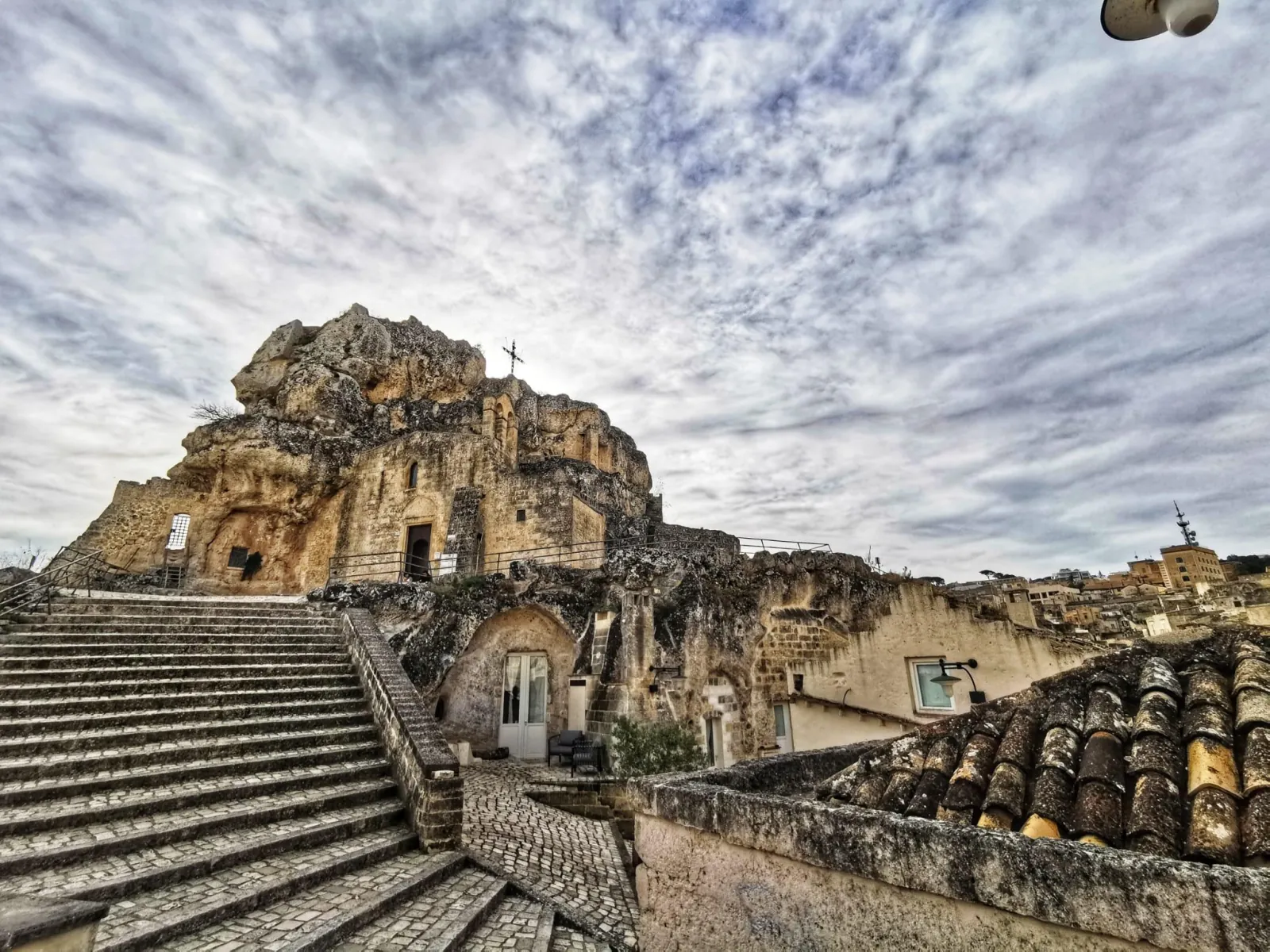 A broad stone staircase leads up to a rock-cut church carved into a rugged outcrop in the Sassi.