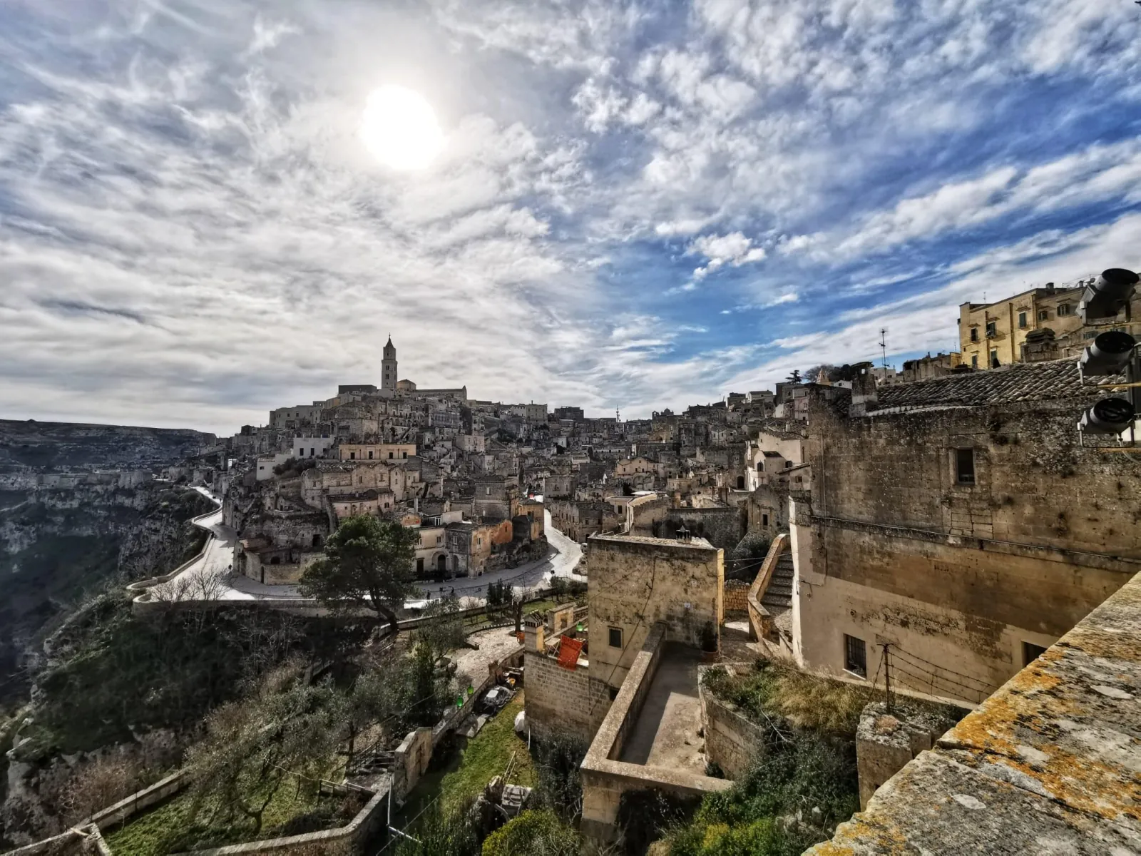 Wide view of Matera's Sassi, terraces and cathedral bell tower above the gorge under a bright sun.