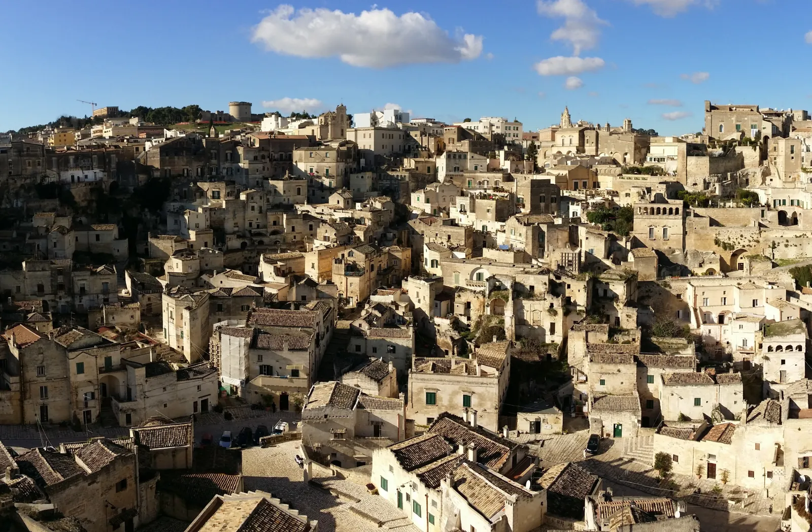 Aerial view of densely packed stone houses and terracotta roofs of the Sassi di Matera under a blue sky.