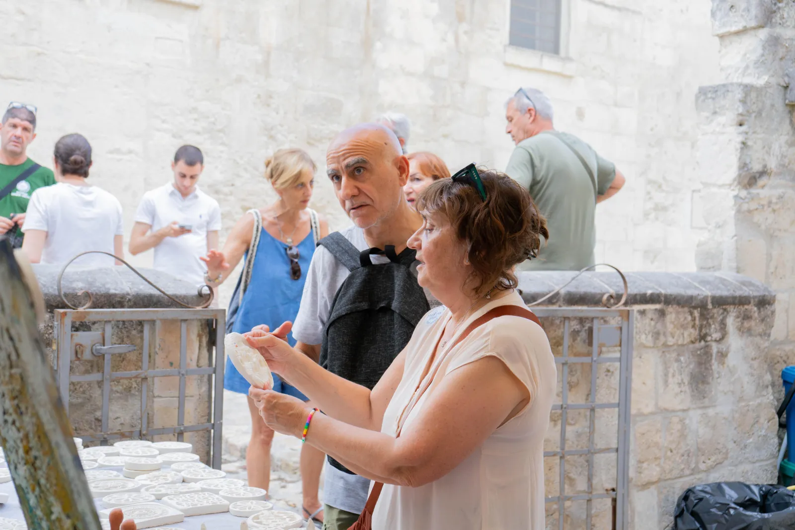 A guide in a beige top explains something to a group beside an iron gate in a Sassi lane.