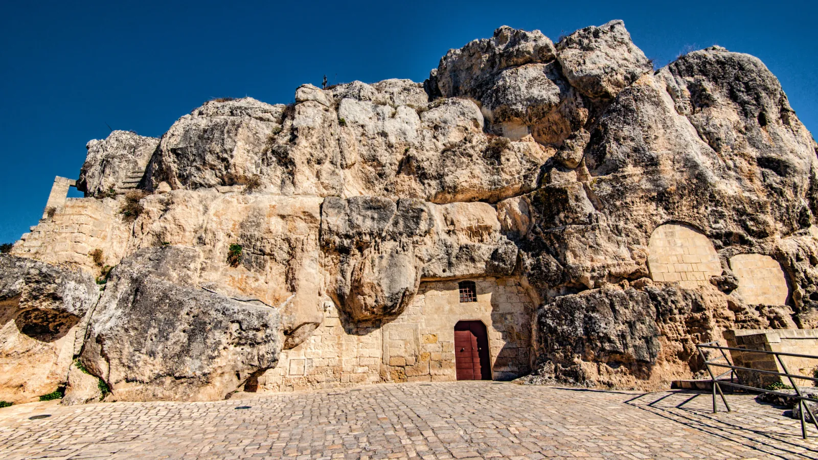 A rocky limestone outcrop in Matera with a red wooden door and arched openings carved into the stone.