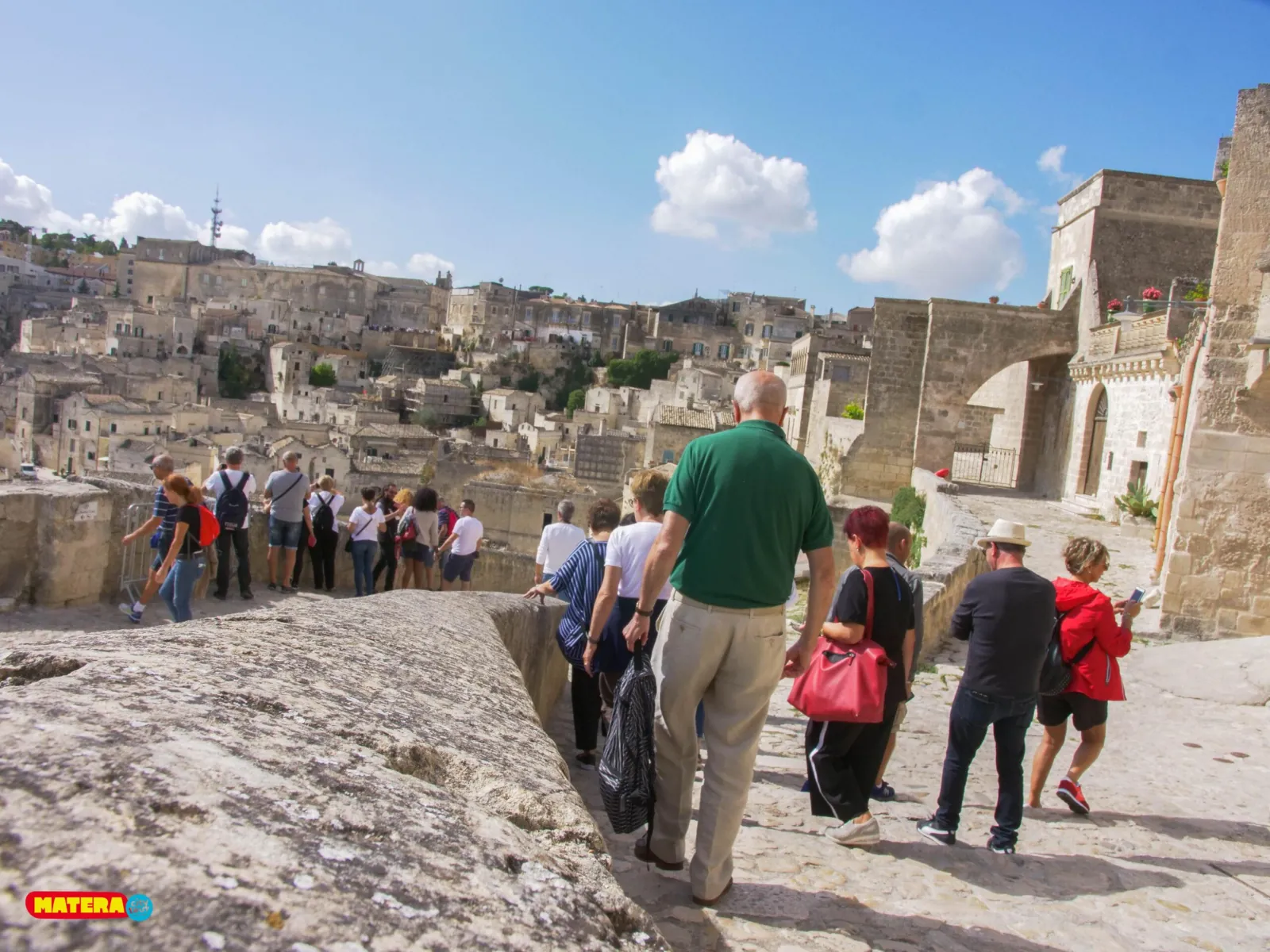 A group follows a guide along a stone wall above the Sassi, with the old town beyond.