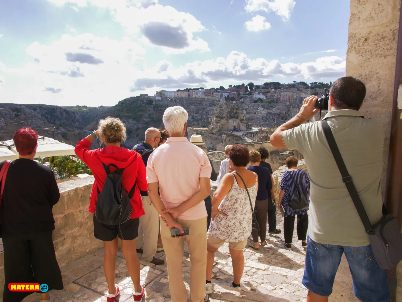 Visitors line up at a stone parapet, photographing the gorge and the Sassi from a terrace in Matera.