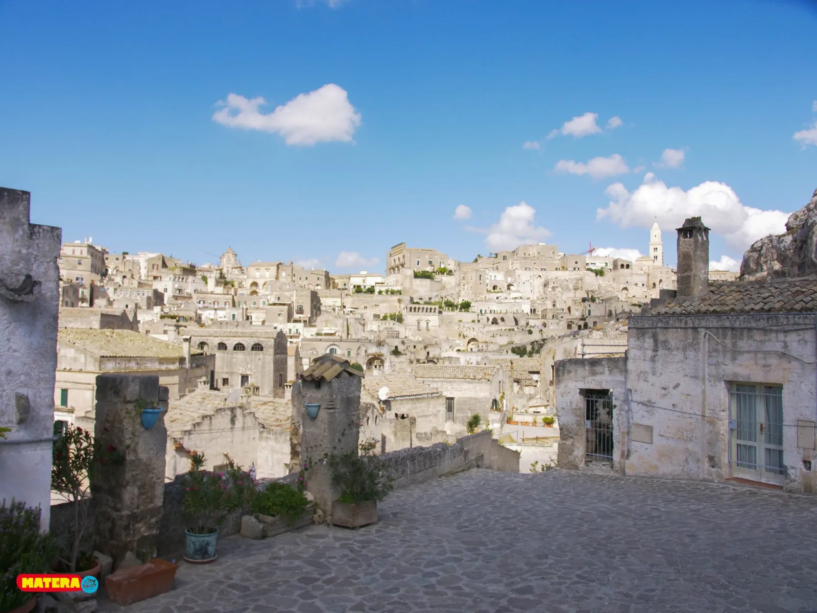 A quiet paved terrace with potted plants looks out over the pale stone houses of the Sassi di Matera.