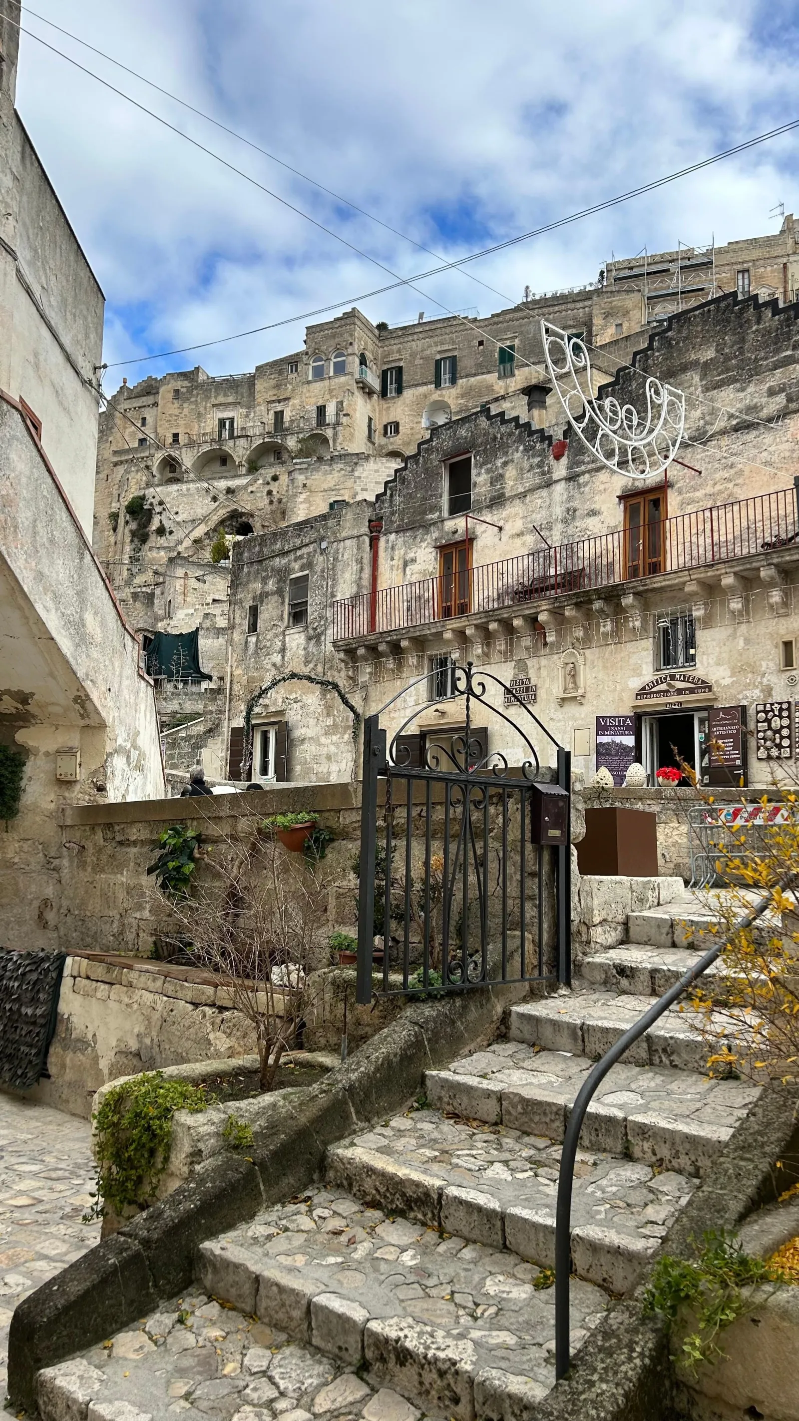 A stone staircase with an iron gate leads up to old stone houses in a Matera lane.