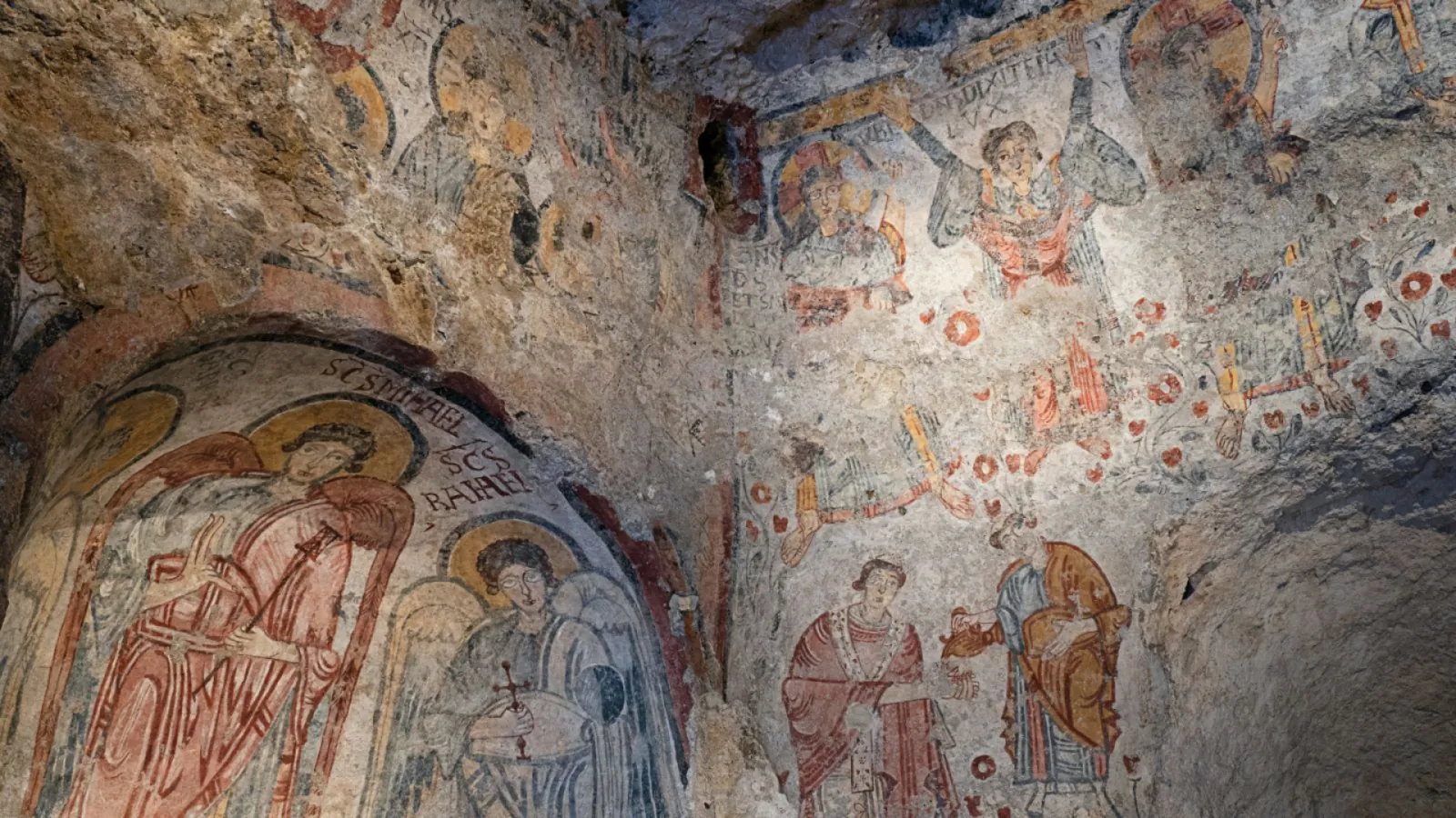 Faded Byzantine-style frescoes of saints painted on the rough rock walls of a cave church in Matera.