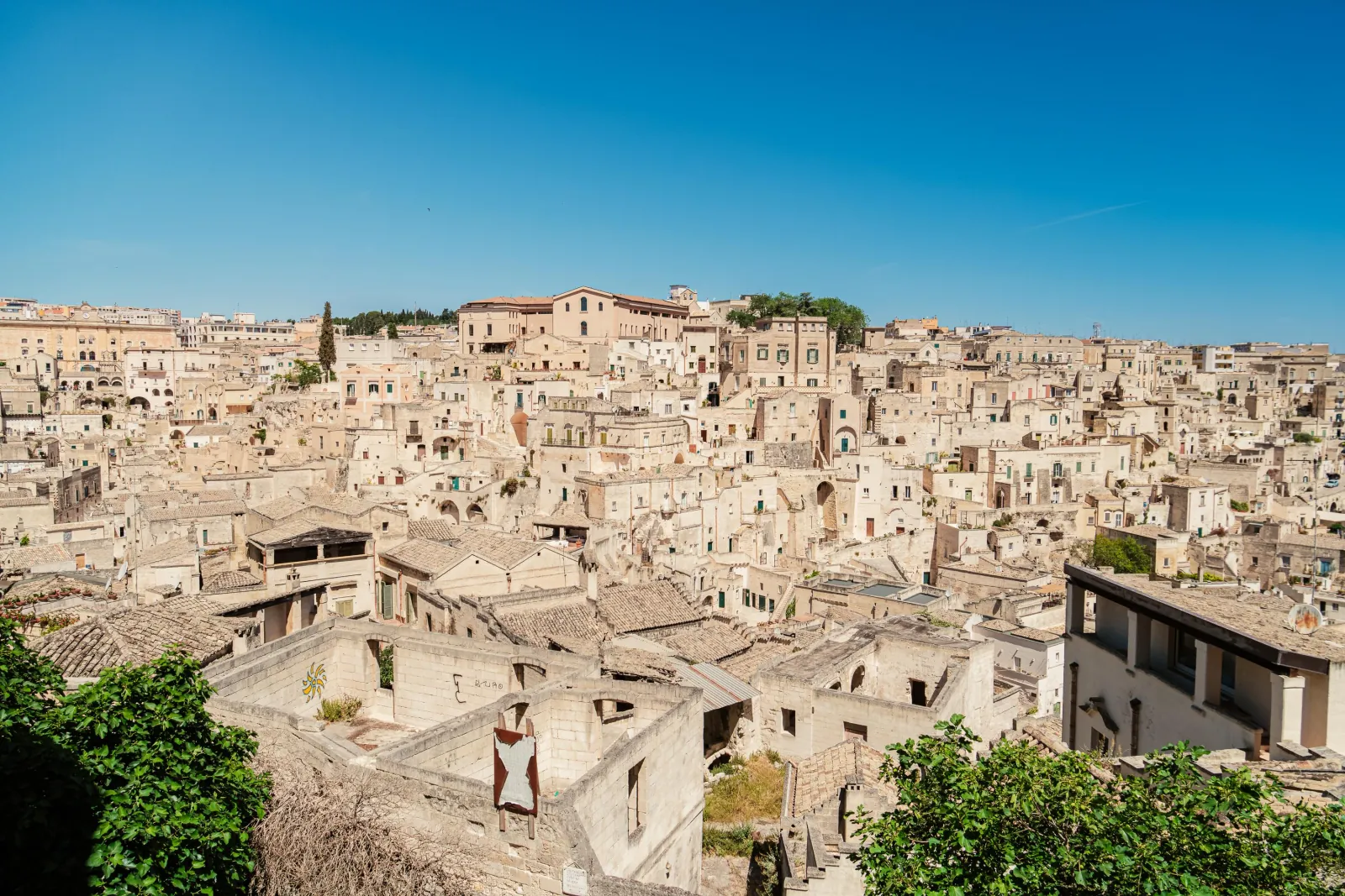 Rooftops and tightly packed stone houses of the Sassi of Matera seen from a hillside under clear skies.