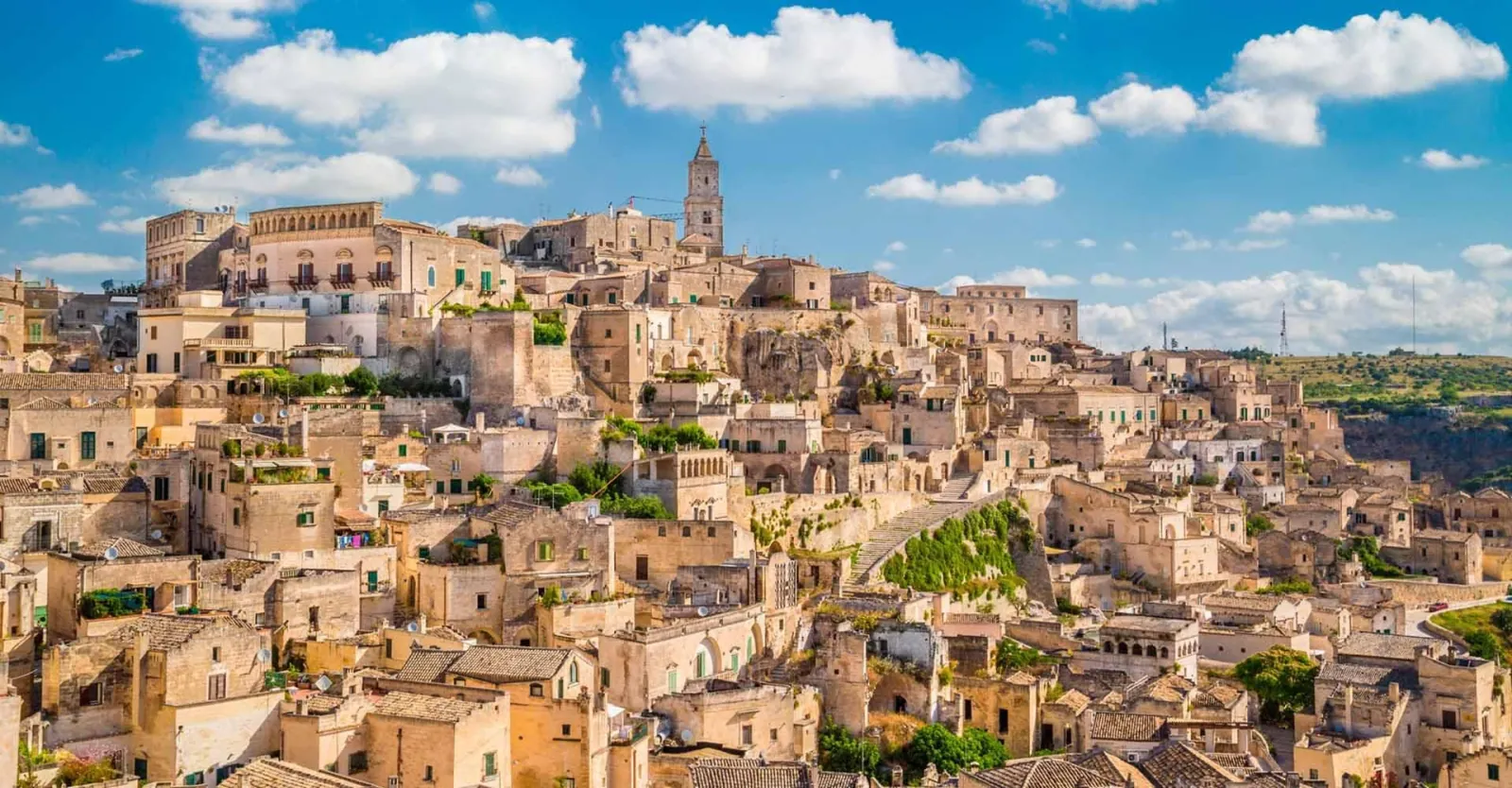 Warm afternoon light on the stone houses and terracotta roofs of Matera, with the cathedral bell tower on the skyline.