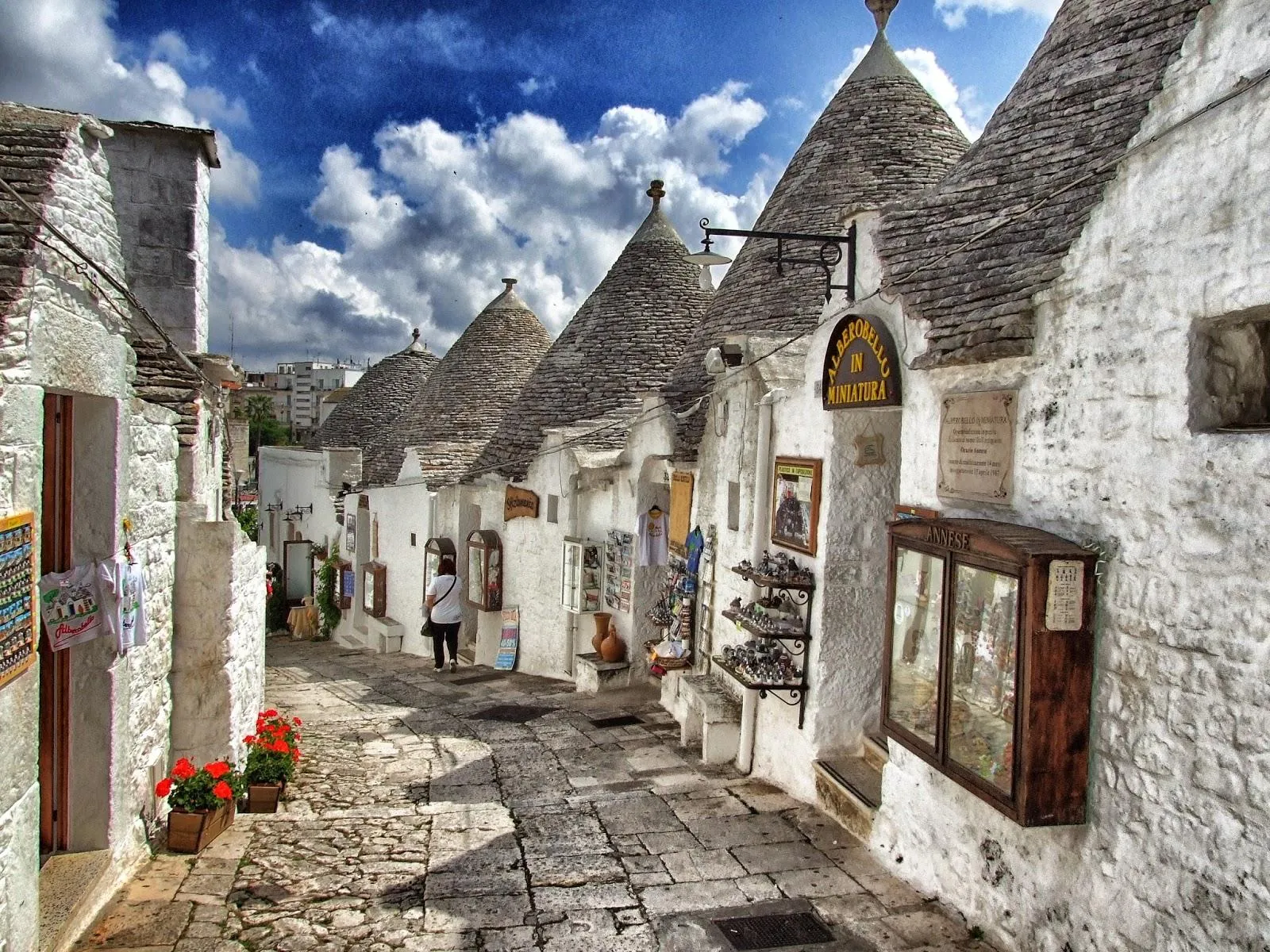 A lane of whitewashed trulli with conical grey stone roofs and small shops in Alberobello.