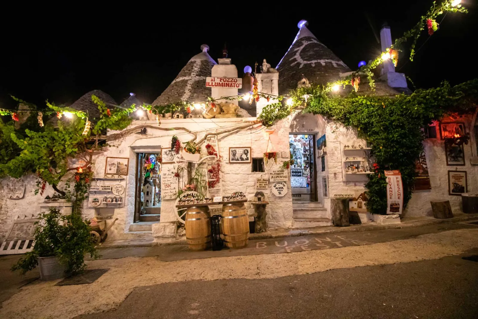 Trulli houses in Alberobello lit with string lights and draped in vines and plants at night.